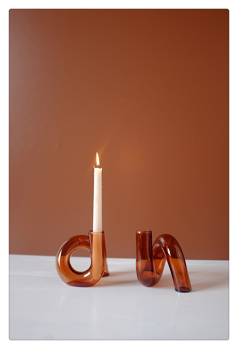 Sculptural amber glass candle holder with lit taper candle against a warm terracotta backdrop