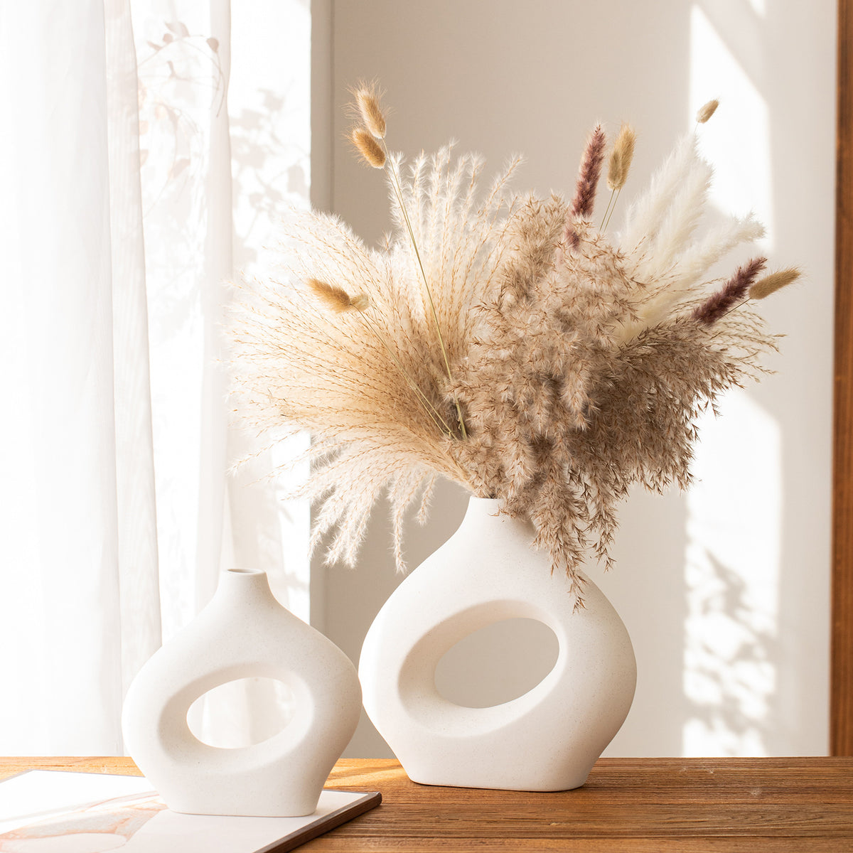 White sculptural hollow vases with dried pampas in a sunlit room
