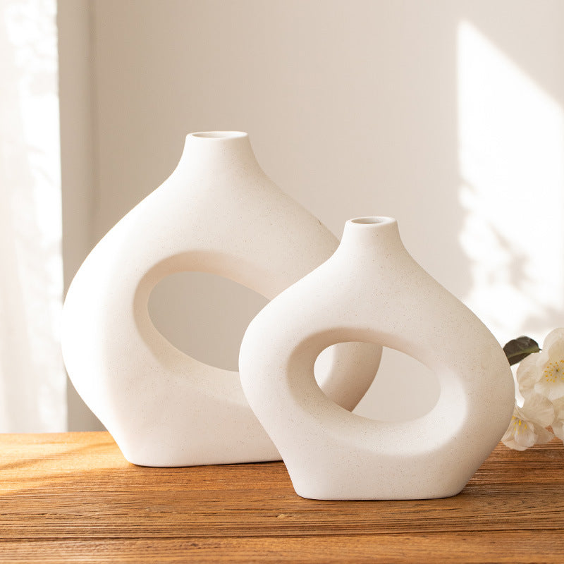 Two matte white hollow ceramic vases on a wooden shelf