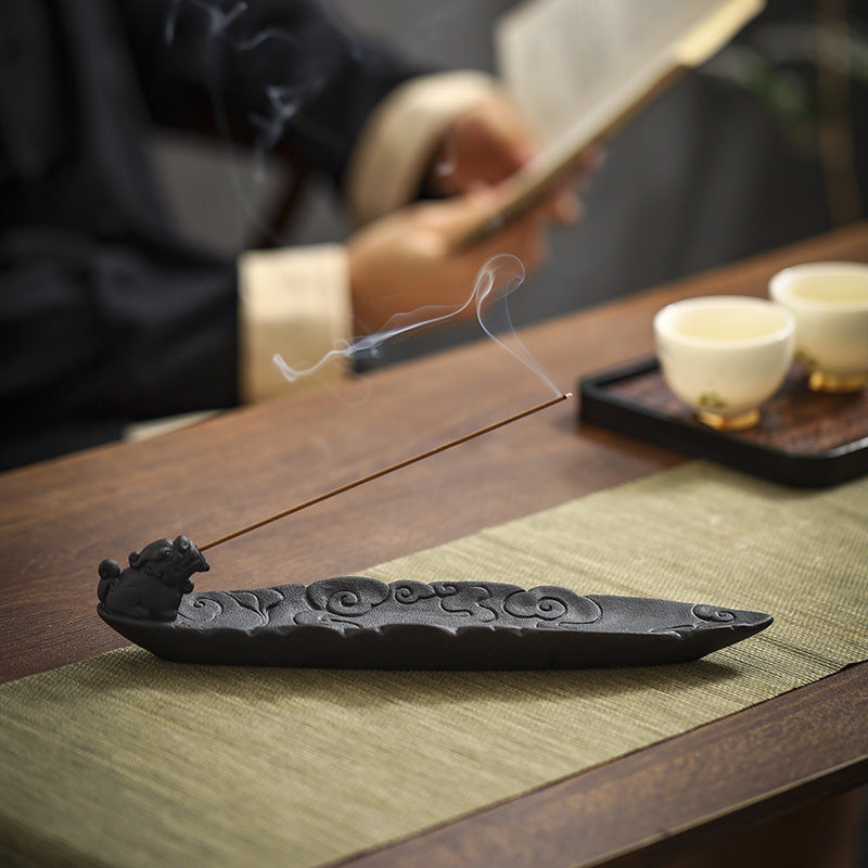 Black ceramic incense stick holder with carved cloud pattern and burning incense stick